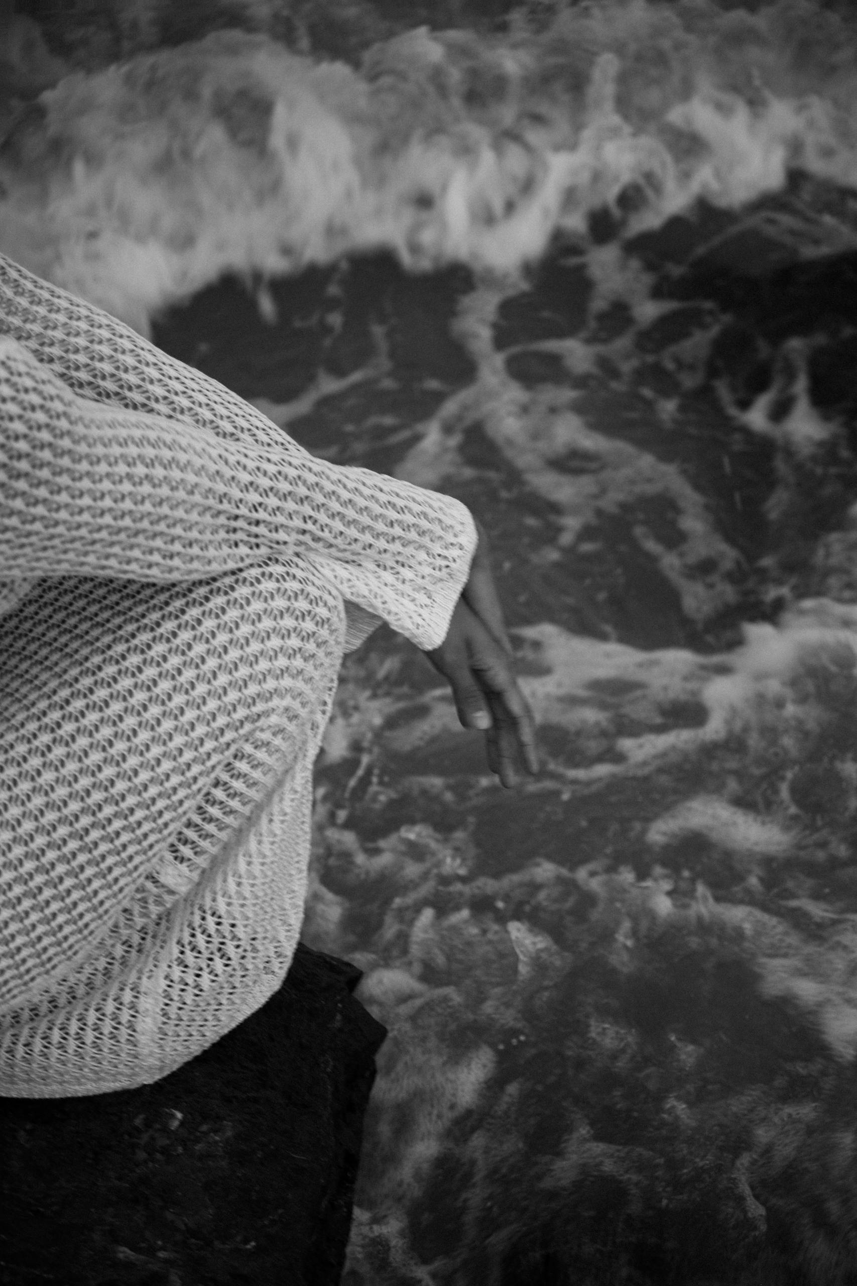A person in a knit sweater sits by the ocean, capturing a serene and introspective moment.