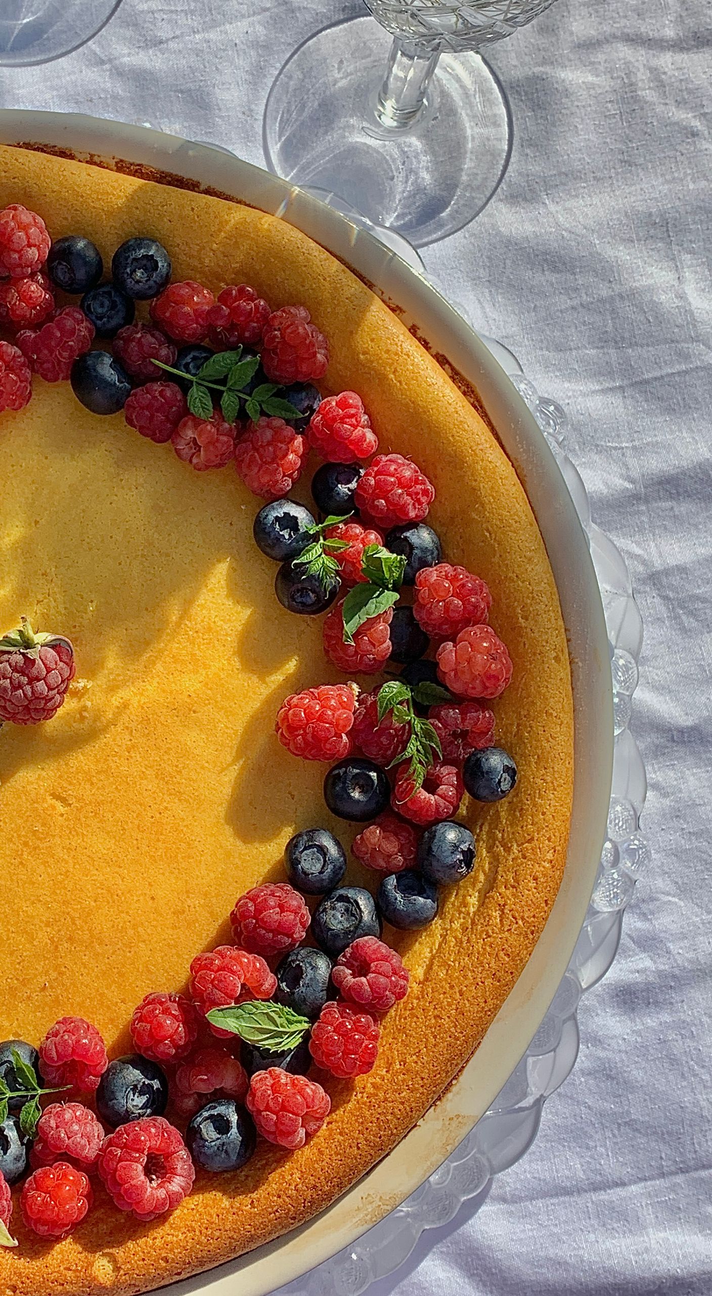 A tempting cheesecake topped with fresh raspberries and blueberries on a sunny table setup.