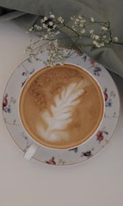 Top view of a cappuccino in a floral cup with latte art and delicate flowers.