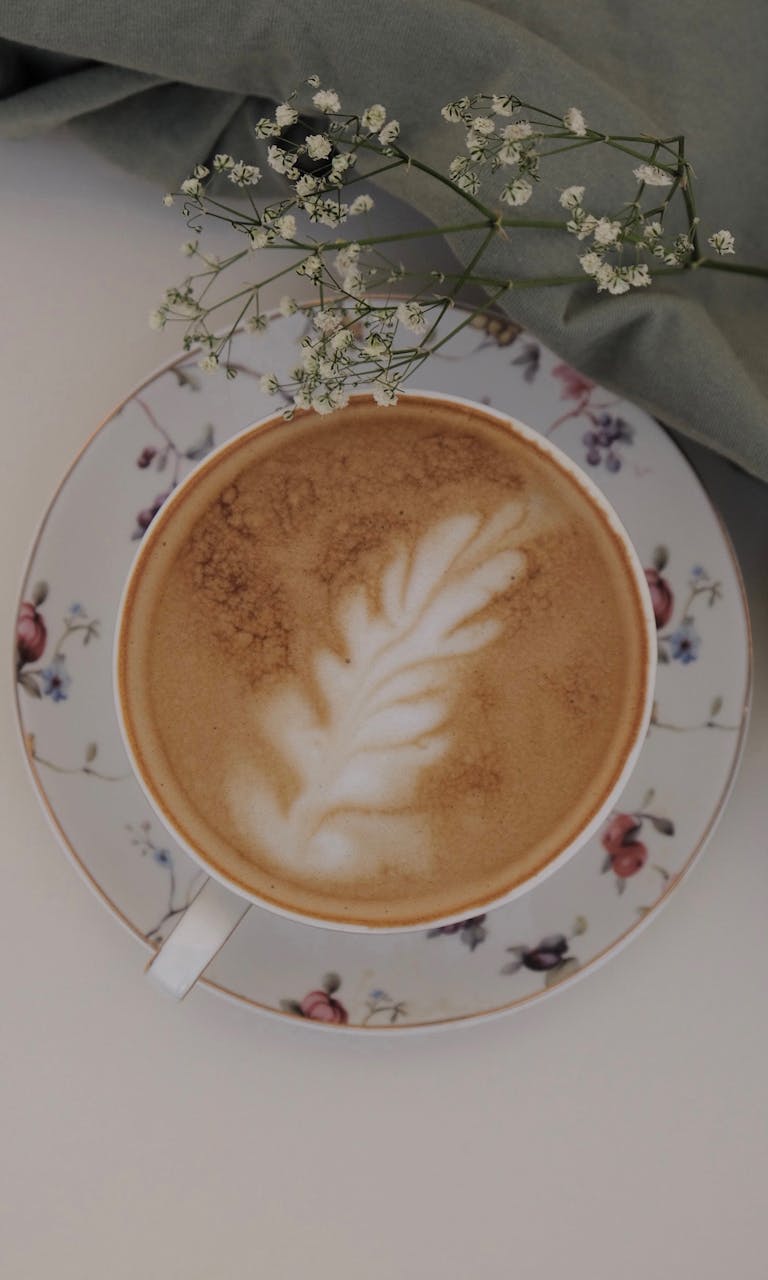 Top view of a cappuccino in a floral cup with latte art and delicate flowers.