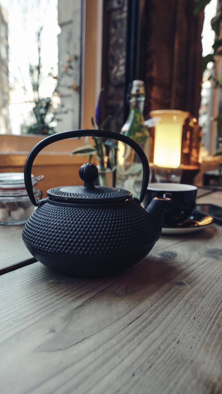A vintage cast iron teapot on a wooden table in a warm, rustic cafe setting.