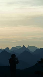 Silhouette of a person photographing scenic mountain ranges during dusk.