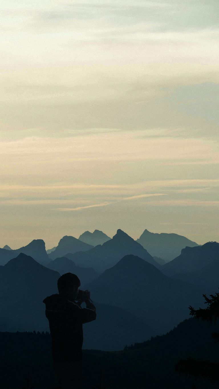 Silhouette of a person photographing scenic mountain ranges during dusk.